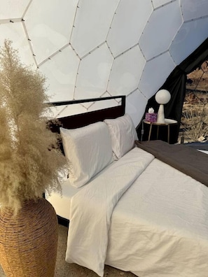 A bed with white bedding, a black headboard, and a woven basket with pampas grass. - Unique and Pet Friendly Glamping Dome with Views of Big Bend National Park, Perfect for a Texas Glamping Getaway (Terlingua)
