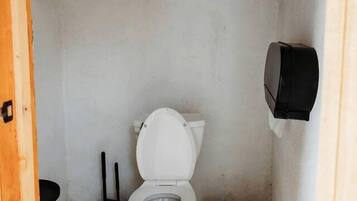 Casa de banho pequena e compacta com sanita, bidé, um cesto de lixo e um distribuidor de papel de parede.