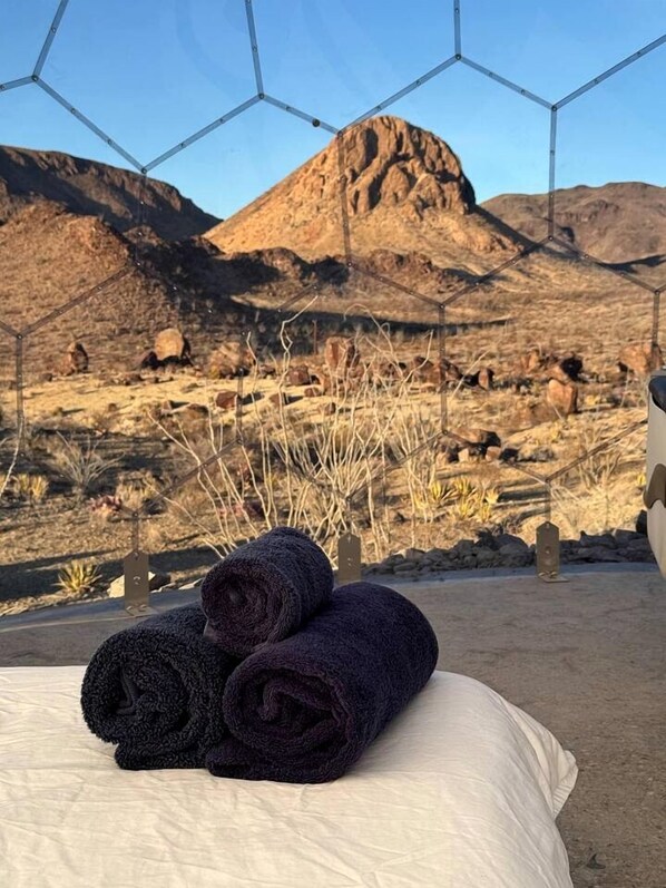 A bed with rolled towels and a view of a mountainous landscape through a geometric window structure.