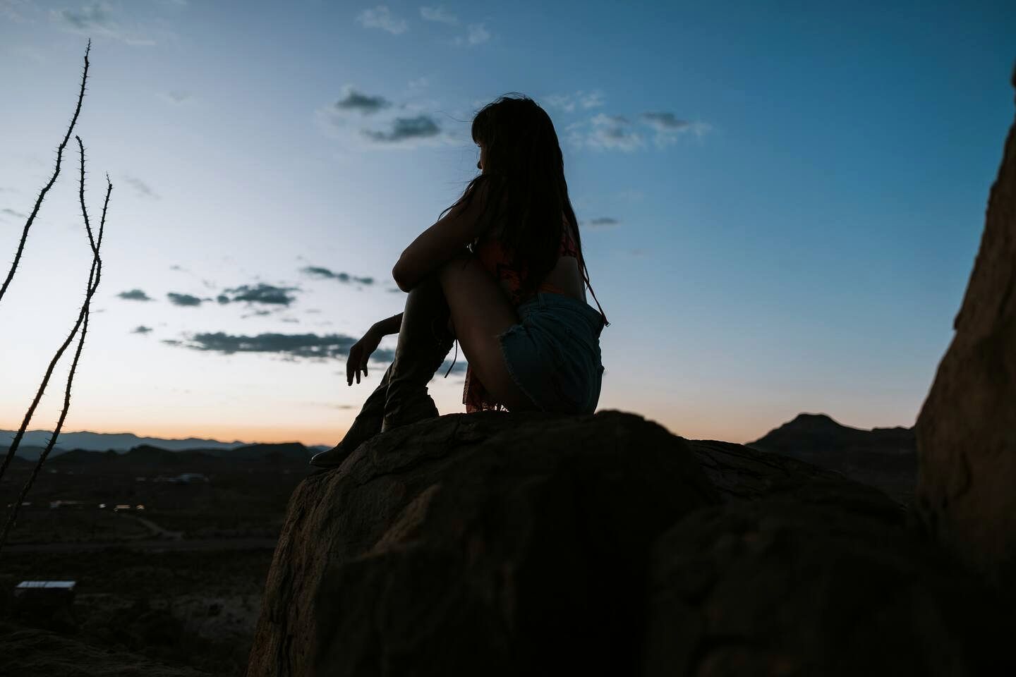Una persona seduta su una roccia, con un cielo sereno sullo sfondo.