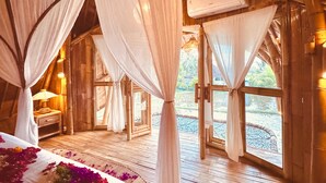 A room with a bed, white curtains, and a wooden floor.