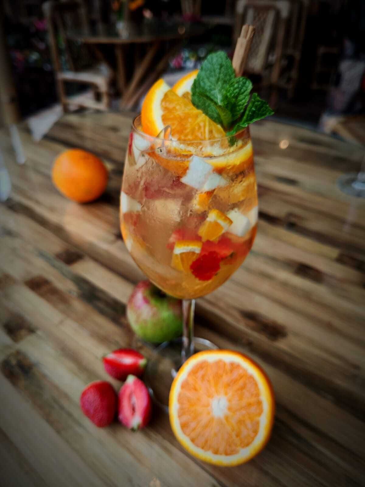 Un verre de cocktail, garni de tranches de fruits et de menthe, sur une table en bois.