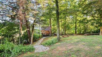 A rustic cabin with a stone pathway leading to it, surrounded by dense forest.