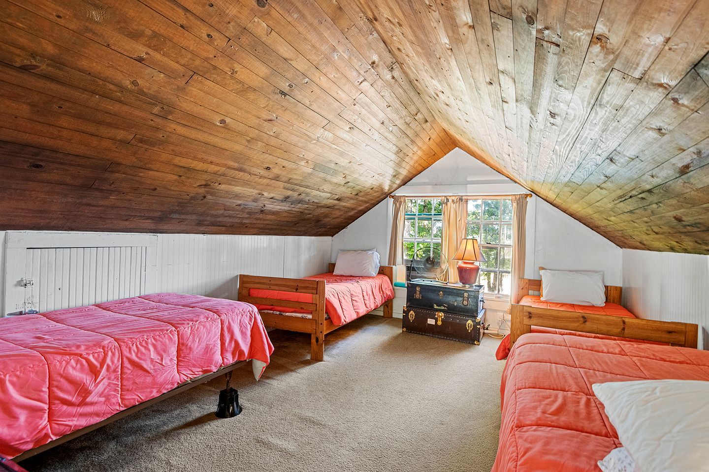 A cozy attic bedroom with two wooden beds, a trunk, and a window with curtains.