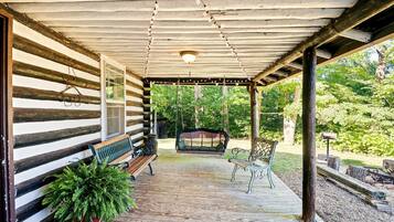 A wooden log cabin with a porch, a swing, and a bench.