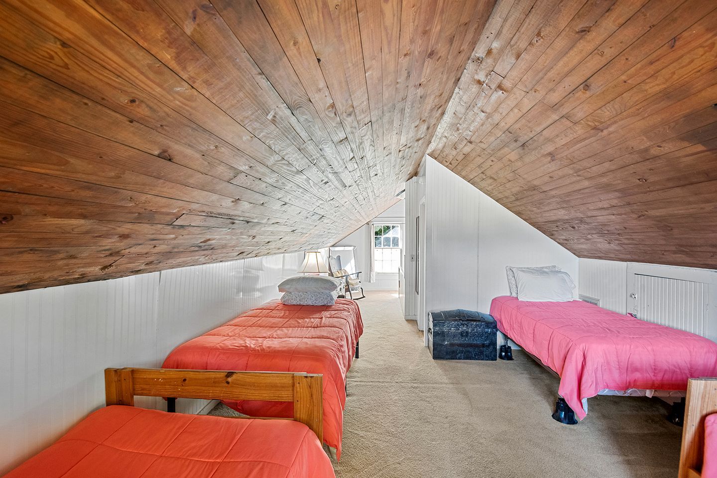 Ein Zimmer mit zwei Betten, Holzbalkendecke und Blick durch eine offene Tür.