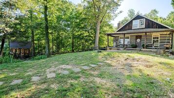 A rustic log cabin with a porch, surrounded by a wooded area.