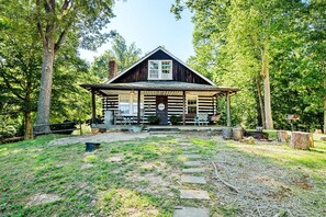 A log cabin with a porch, surrounded by trees.