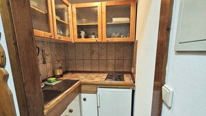 A compact kitchen with wooden cabinets, a small refrigerator, and a tiled floor. - Apartment Gerda (Pappenheim)