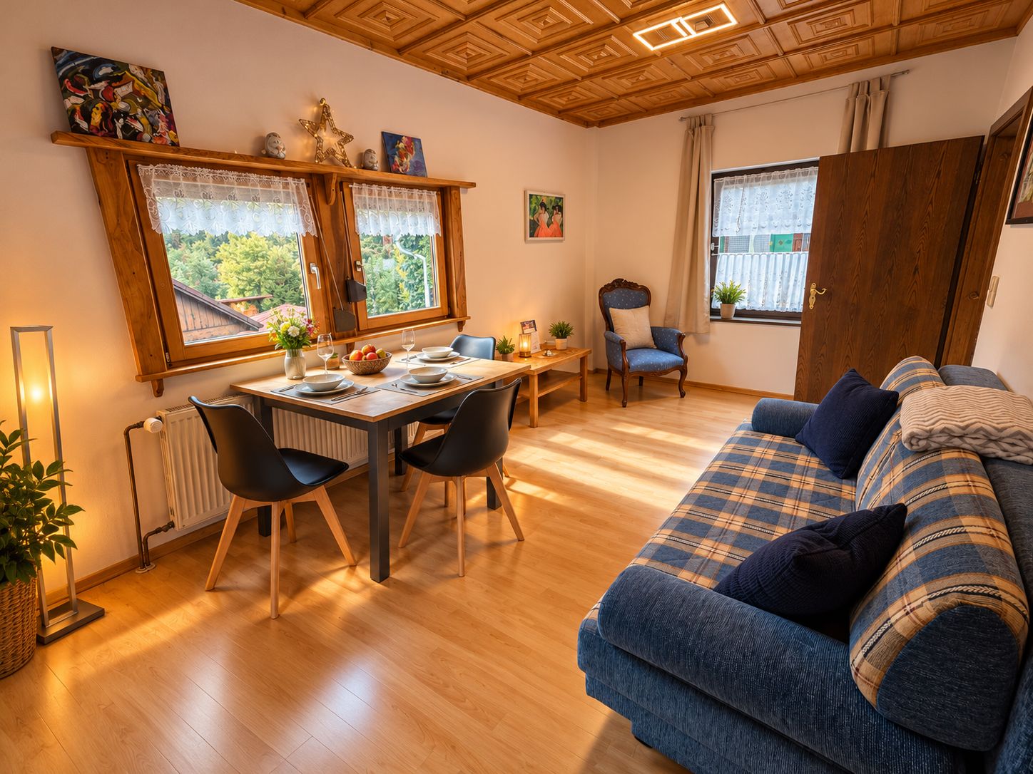 Ein gemütliches Wohnzimmer mit Essbereich, Holzboden, einem blauen Sofa und einem Fenster mit Blick auf Grünflächen.