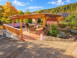 A wooden pergola with seating, a horse statue, and a garden with various plants.