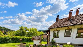 Ein gepflegter Garten mit einer Terrassenfläche, einer kleinen Gartenhütte und einem Haus mit Ziegeldach.