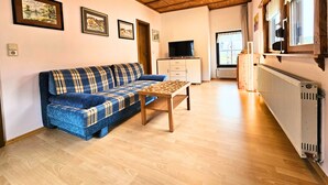A cozy living room with a blue plaid sofa, a wooden coffee table, and a television on a cabinet. - Apartment Gerda (Pappenheim)
