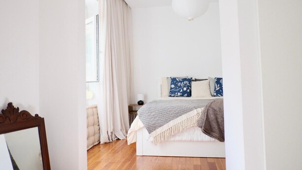 Un dormitorio con cama, mesita de noche, lámpara y ventana con cortinas.