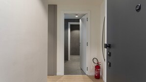 Un pasillo con un extintor en el suelo, una puerta a la derecha y una pared de azulejos al fondo.
