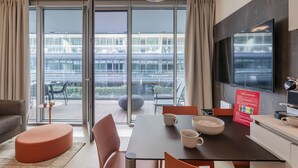 Habitación de hotel moderna con zona de comedor, sofá y un amplio ventanal con vistas a la ciudad.