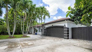 Una propiedad residencial con garaje, entrada para coches y un césped bien cuidado con palmeras.