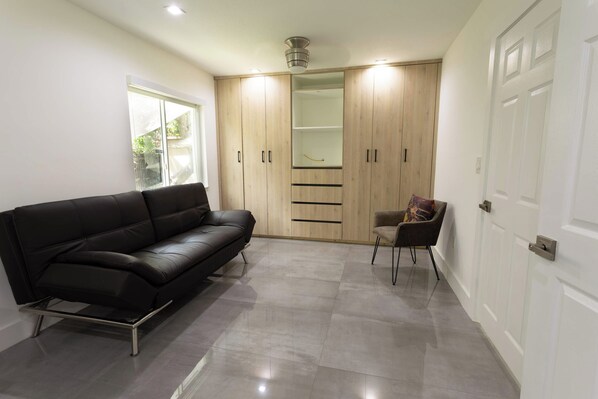 A modern living room with a black leather sofa, a wooden wardrobe, and a small chair. - Tropical Paradise | Boat Parking | Pet Friendly (Miami)