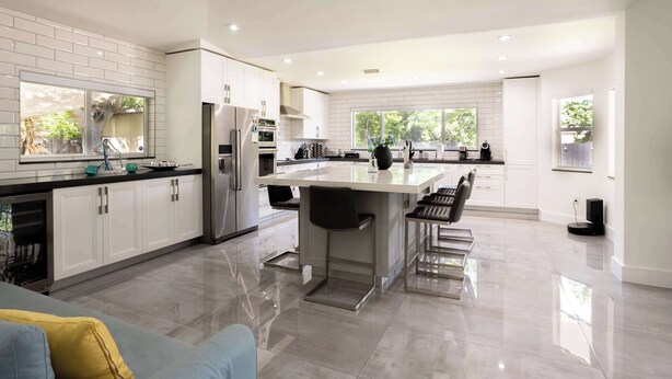 Una cocina moderna con armarios blancos, electrodomésticos de acero inoxidable y una isla central con taburetes de bar.