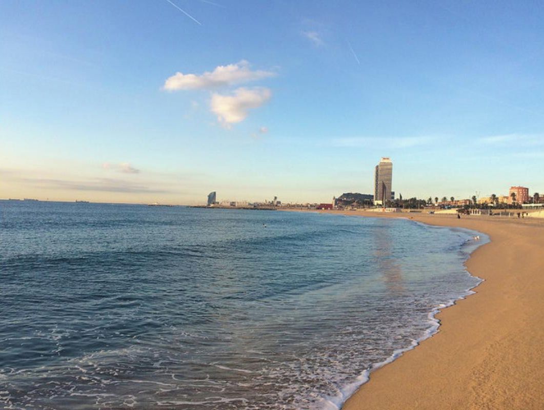 Een strand met een heldere lucht, een zandstrand en een verafgelegen stadsgezicht met een hoog gebouw.