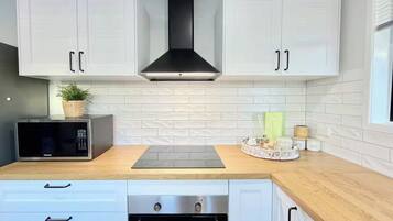 A modern kitchen with white cabinets, a black range hood, a microwave, a built-in oven, and a wooden countertop.