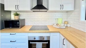 A modern kitchen with white cabinets, a black range hood, a microwave, a built-in oven, and a wooden countertop. - A Sunday Kind of Stay -  Home Near Manly + Shops (Capalaba)
