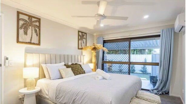 A bedroom with a bed, a nightstand, a ceiling fan, and a window with curtains. - A Sunday Kind of Stay -  Home Near Manly + Shops (Capalaba)