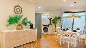 A modern kitchen with a washing machine, dining area with white chairs, and a large woven rug. - A Sunday Kind of Stay -  Home Near Manly + Shops (Capalaba)