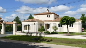 Une maison à deux étages, avec un toit en tuiles, une cour clôturée et une pelouse bien entretenue.