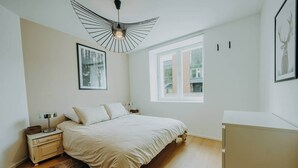 A bedroom with a bed, a nightstand, a lamp, a framed picture, a window, and a ceiling light fixture. - Loft d'Houffalize - by Mansio (Houffalize)