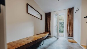 A hallway with a wooden bench, a door leading outside, and a view of greenery through the window. - Loft d'Houffalize - by Mansio (Houffalize)