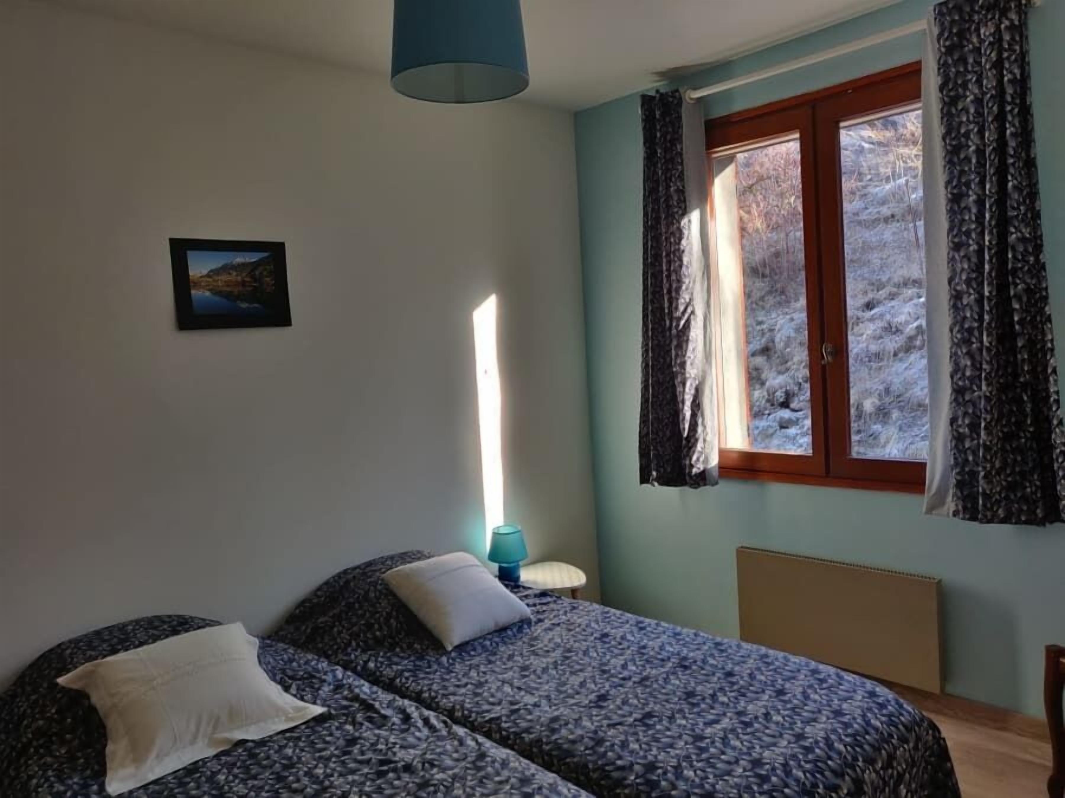 A bedroom with two beds, a window with curtains, a lamp, and a picture on the wall.