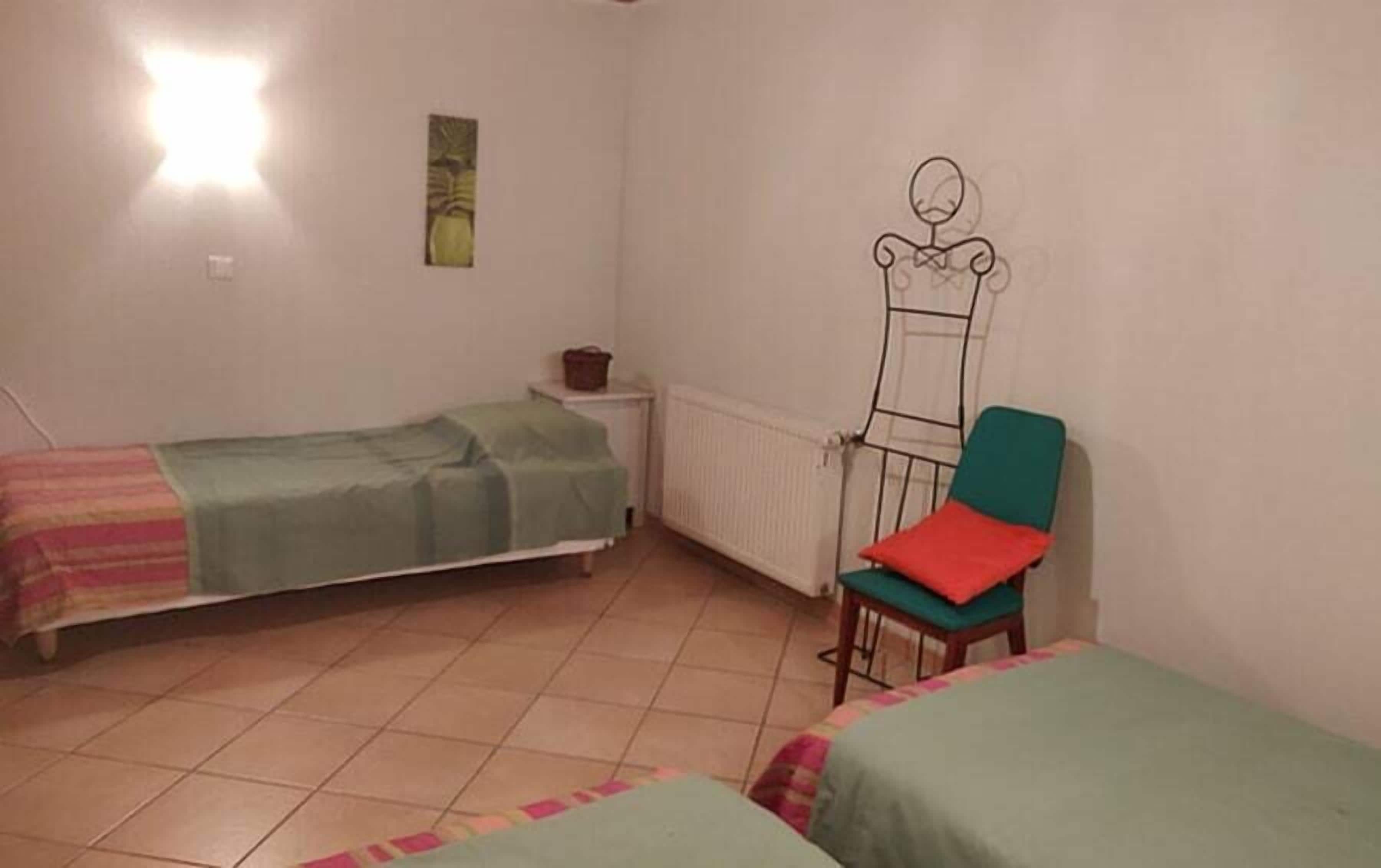 Una habitación pequeña y sencilla con dos camas individuales, una silla y un radiador.