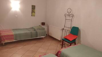 Una habitación pequeña y sencilla con dos camas individuales, una silla y un radiador.