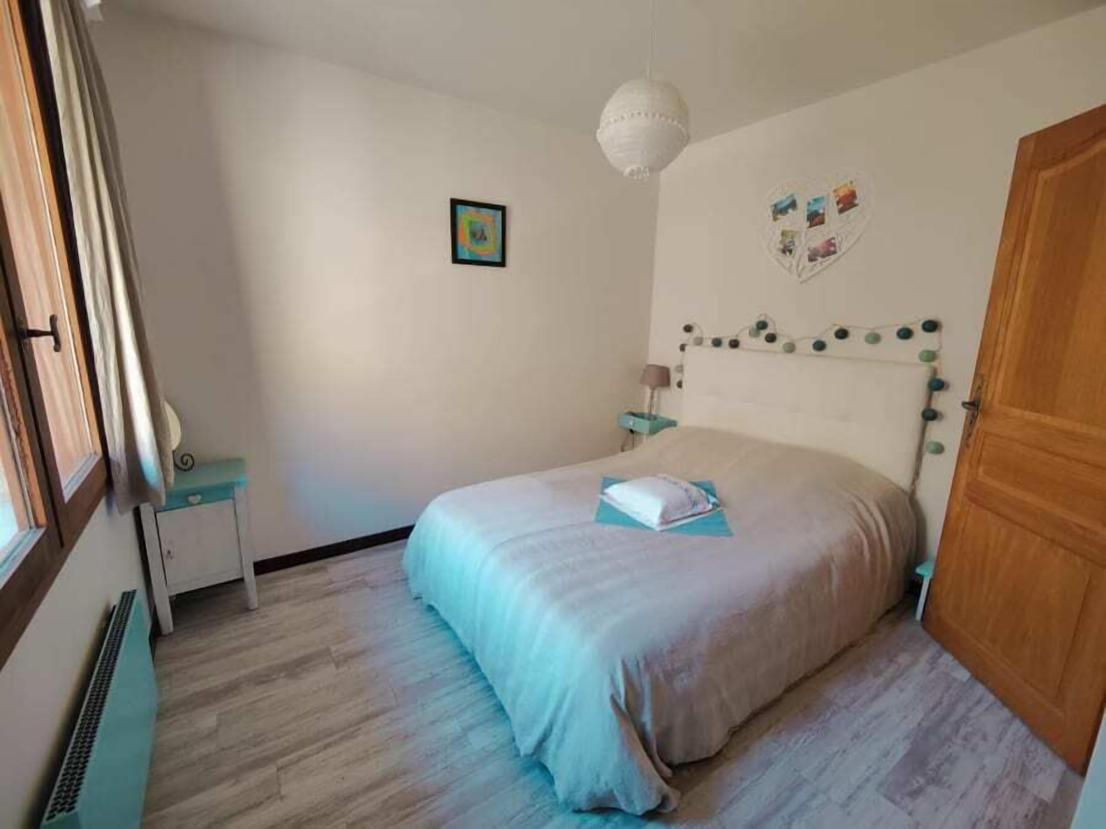 A bedroom with a bed, a bedside table, a lamp, a wall decoration, and a door.