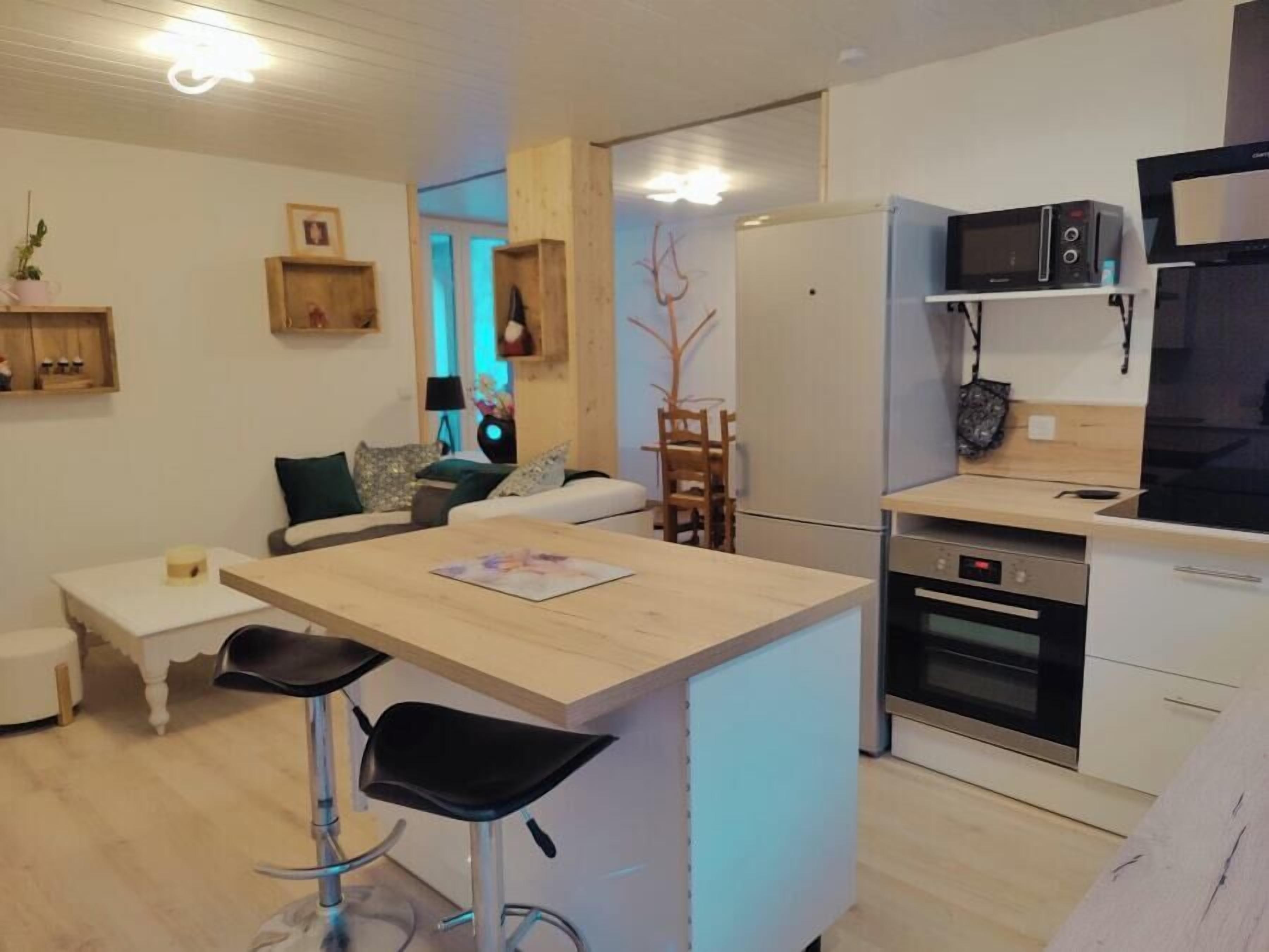 Una cocina moderna con una isla central, taburetes de bar, un refrigerador, microondas, horno y un comedor con sillas.
