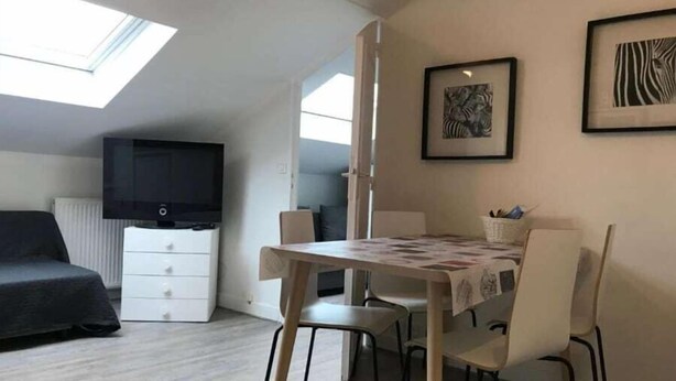 Egy modern, jól megvilágított szoba, ahol egy emeletes ágy, egy síkképernyős televízió, egy étkezőasztal székekkel, valamint két, keretbe foglalt műalkotás található a falakon.