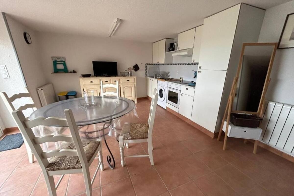 Une cuisine compacte comprenant une table de salle à manger ronde, des chaises, un lave-linge et un téléviseur.