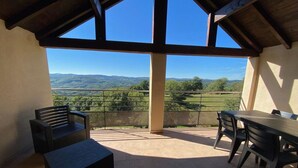 Une terrasse offrant une vue sur des collines verdoyantes, une table en bois et deux bancs.