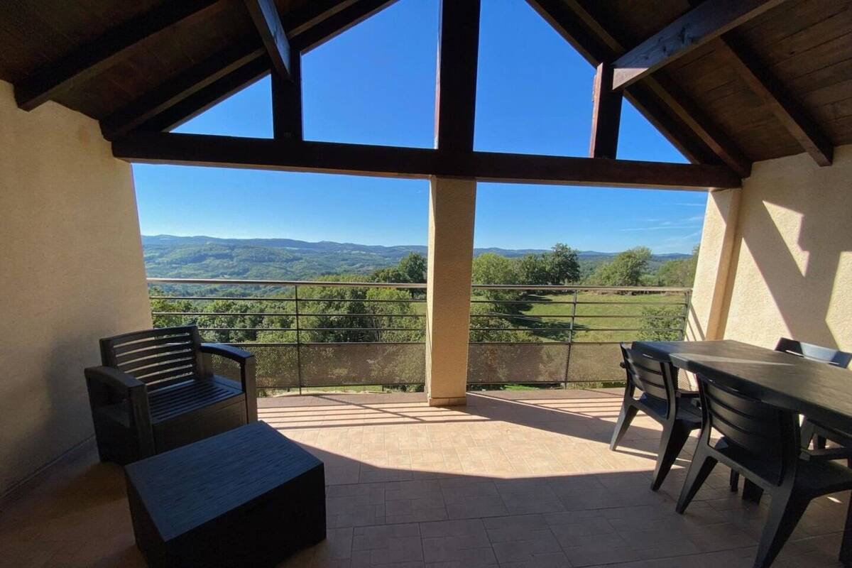 Une terrasse offrant une vue sur des collines verdoyantes, une table en bois et deux bancs.