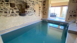 Une piscine intérieure avec des murs en pierre et une vue dégagée sur l’espace piscine.