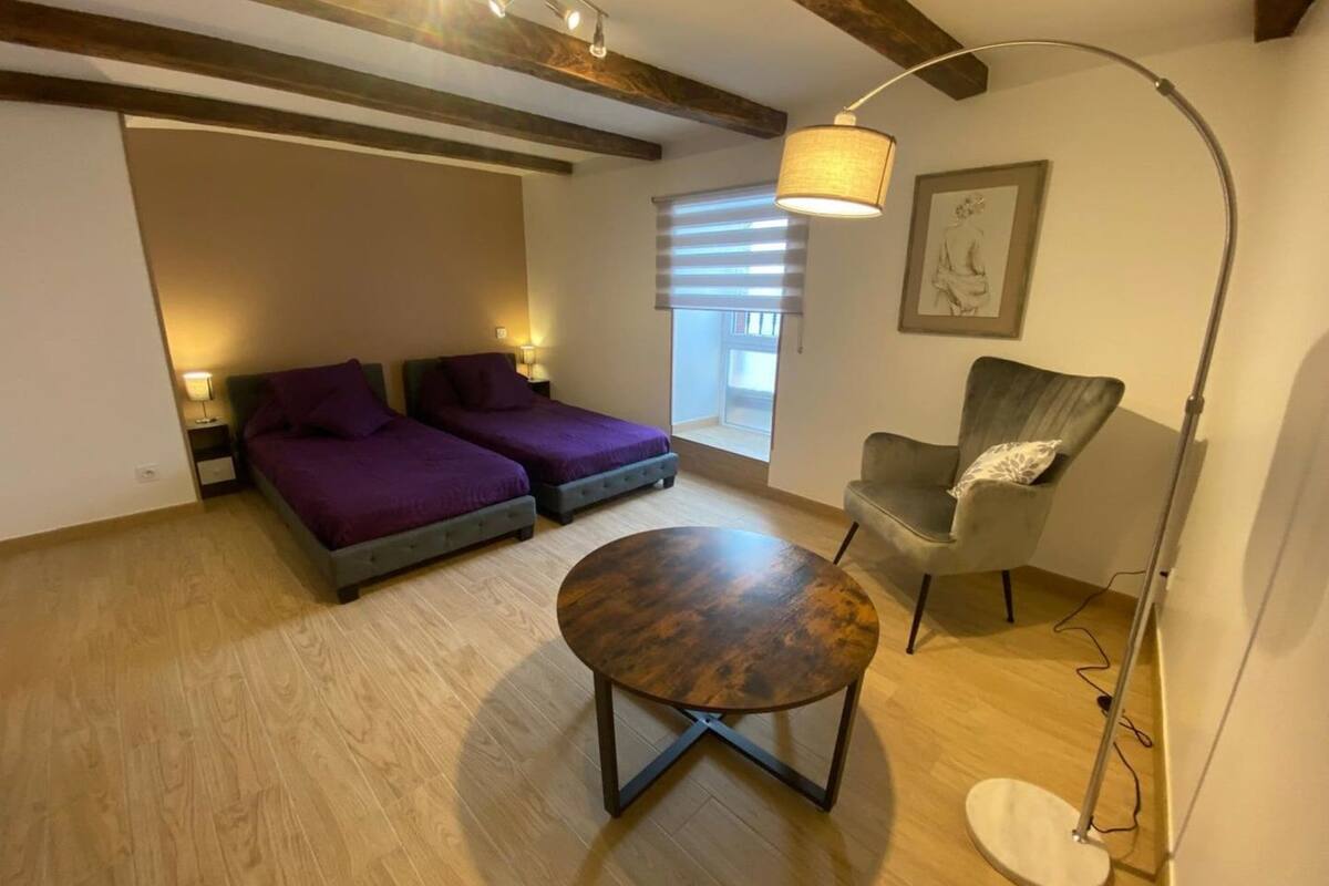 Une chambre avec deux lits, une table ronde, une chaise, un lampadaire et une fenêtre avec des stores.