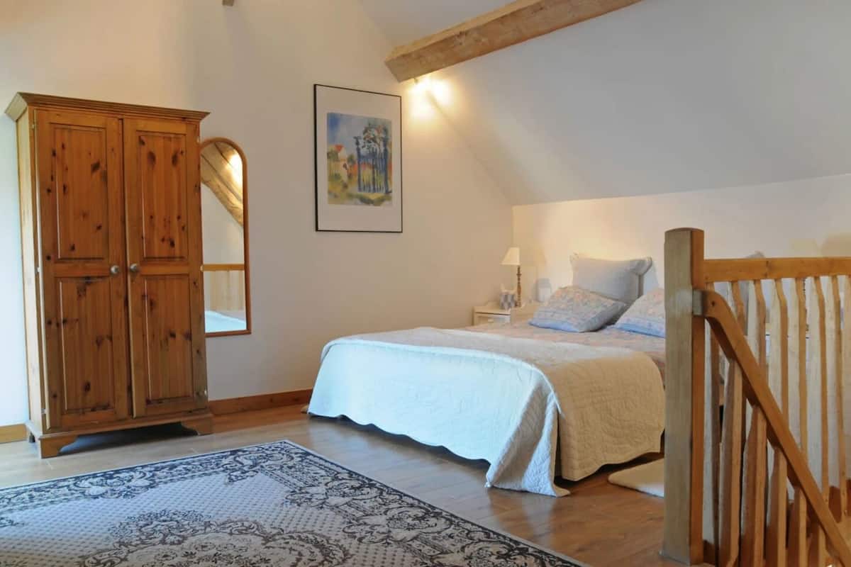 A bedroom with a bed, a wooden wardrobe, a mirror, and a painting on the wall.