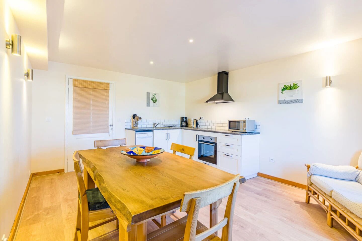 A compact kitchen with white cabinets, a microwave, and a stove. There is a wooden dining table with chairs and a bowl on it.