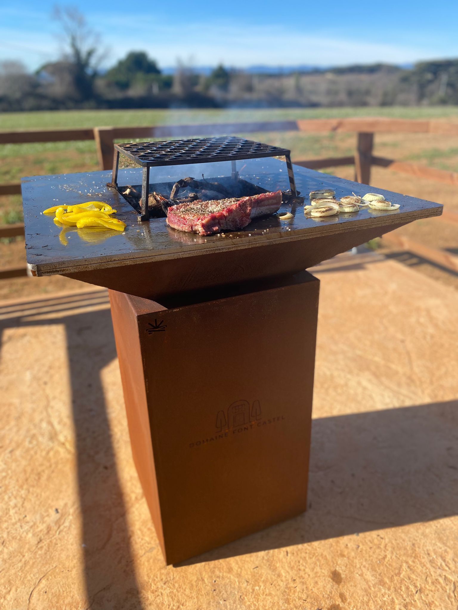 Un barbecue portable avec un steak et des légumes, posé sur un support en bois à l’extérieur.