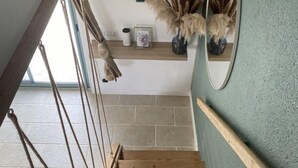 Un escalier avec une rampe en bois, un miroir fixé au mur et une étagère ornée d’objets décoratifs.