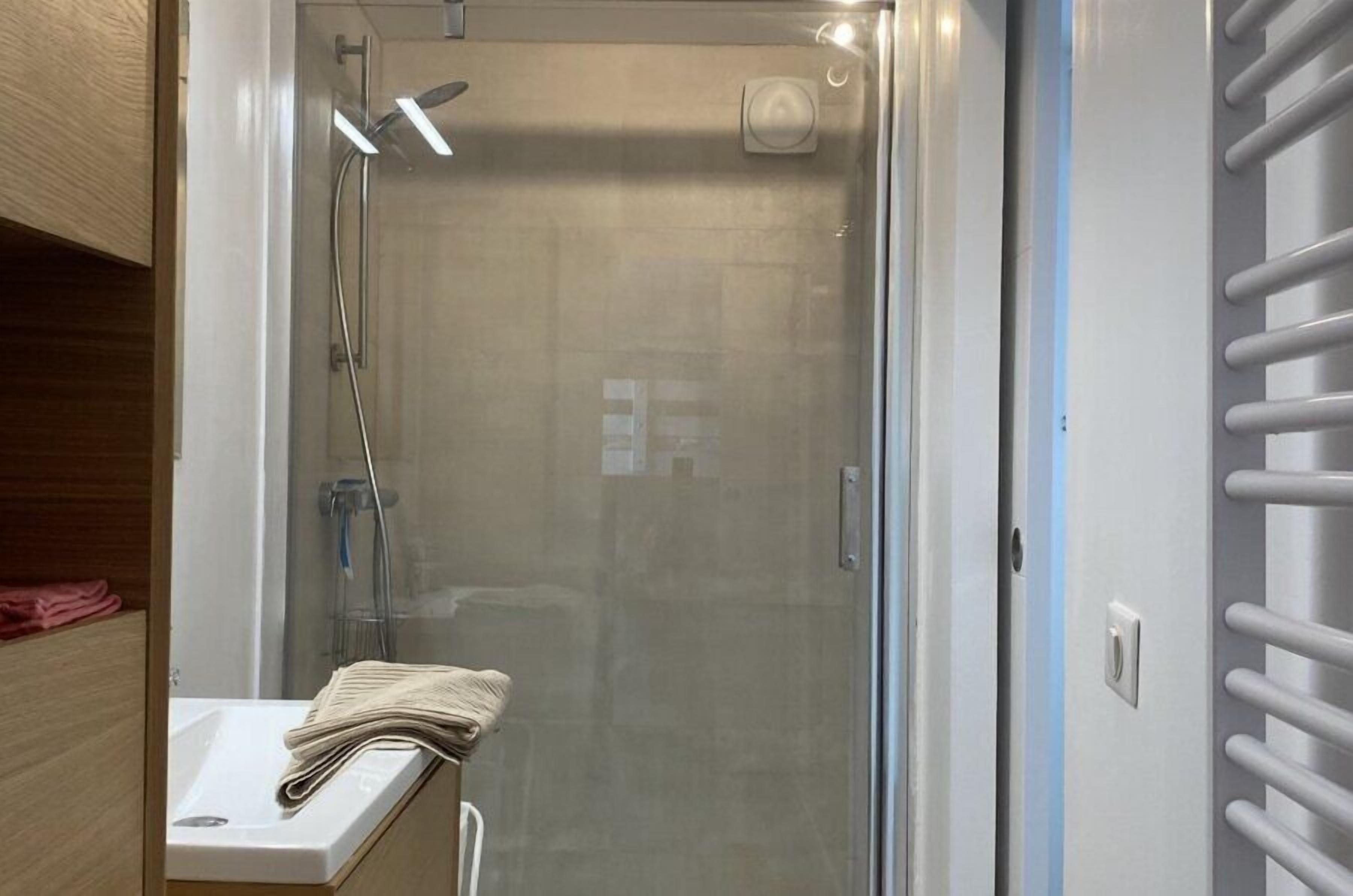 A modern bathroom with a glass-enclosed shower, a white sink, and a towel rack.