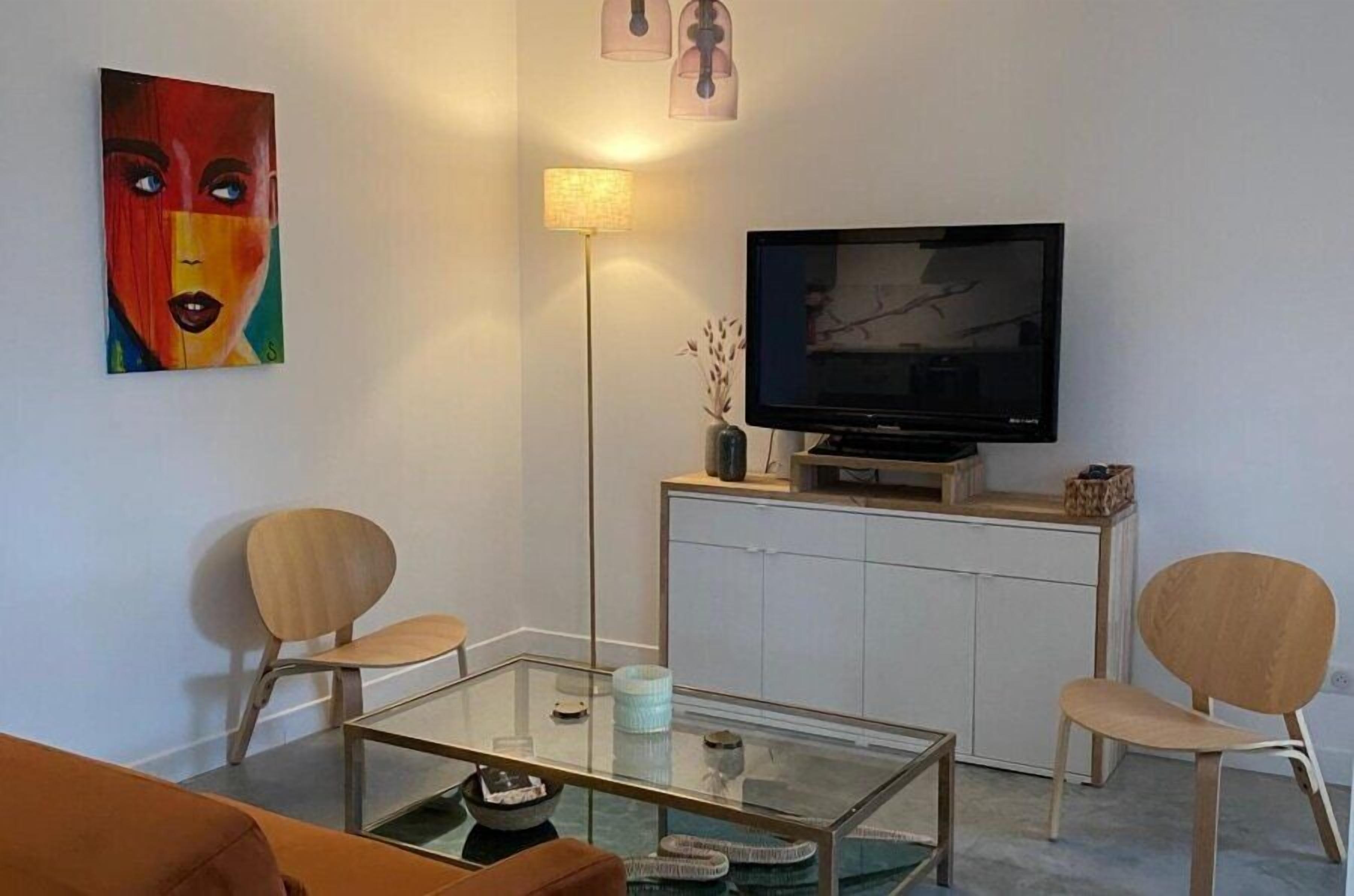 Ein modernes Wohnzimmer mit einem Glastisch, zwei Holzstühlen, einem Flachbildfernseher, einem Schrank und einem Gemälde an der Wand.