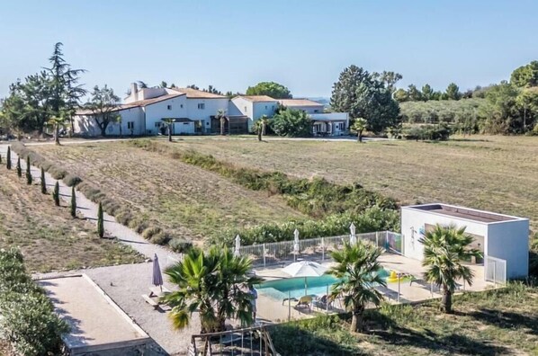 Une grande maison avec une piscine, entourée d’un jardin clos et de palmiers.