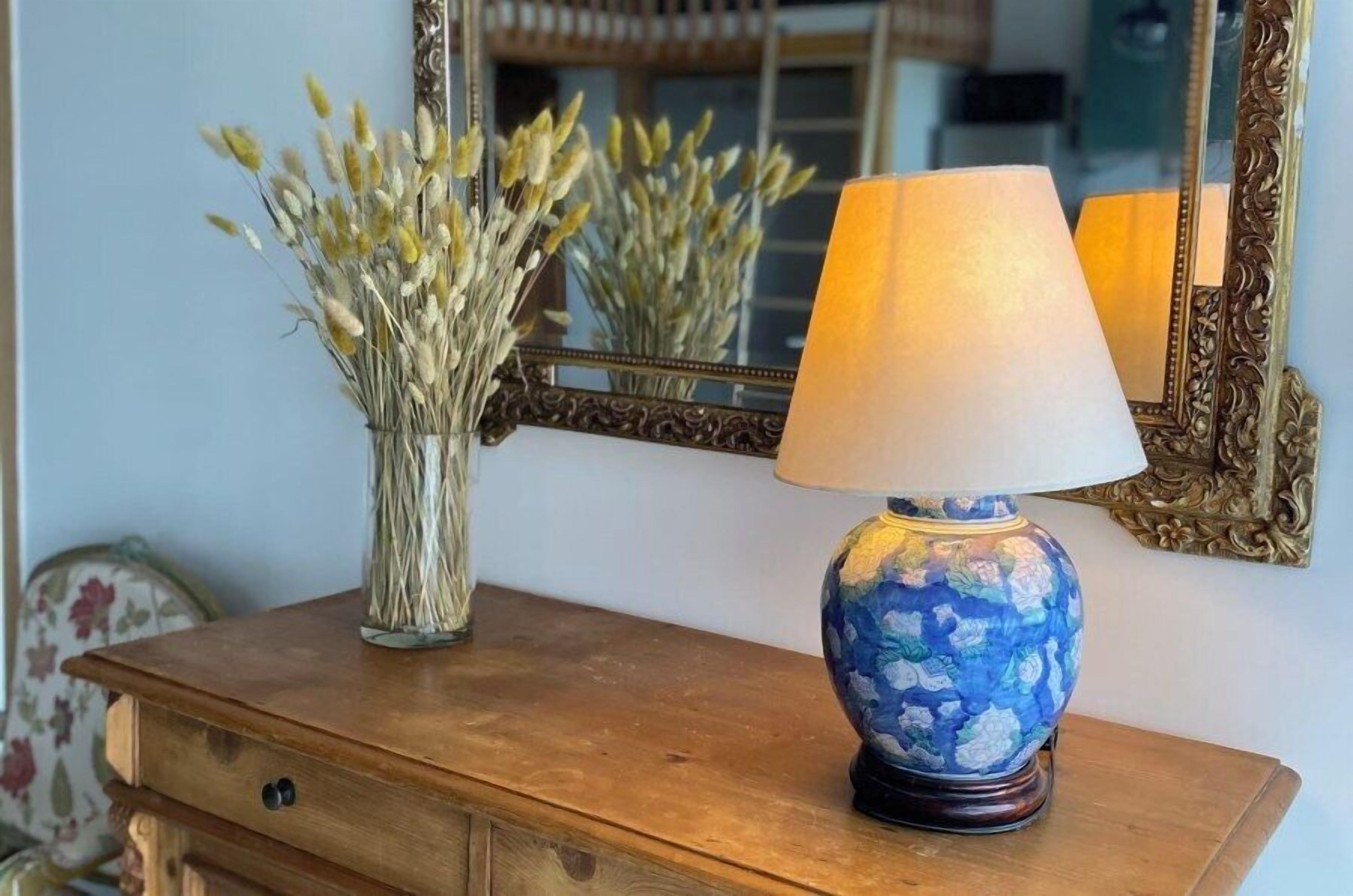 Un aparador de madera con un jarrón de flores secas y una lámpara de diseño azul y blanco.